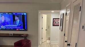 A living room with a flat-screen TV, a red chair, a coffee table, and a hallway leading to a door.