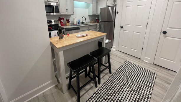 A compact kitchen with white cabinets, a stainless steel refrigerator, a microwave, and a sink. There are two black stools at the island counter.