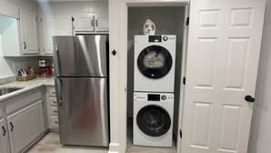 A compact kitchen with a stainless steel refrigerator, a coffee maker, and a washing machine.