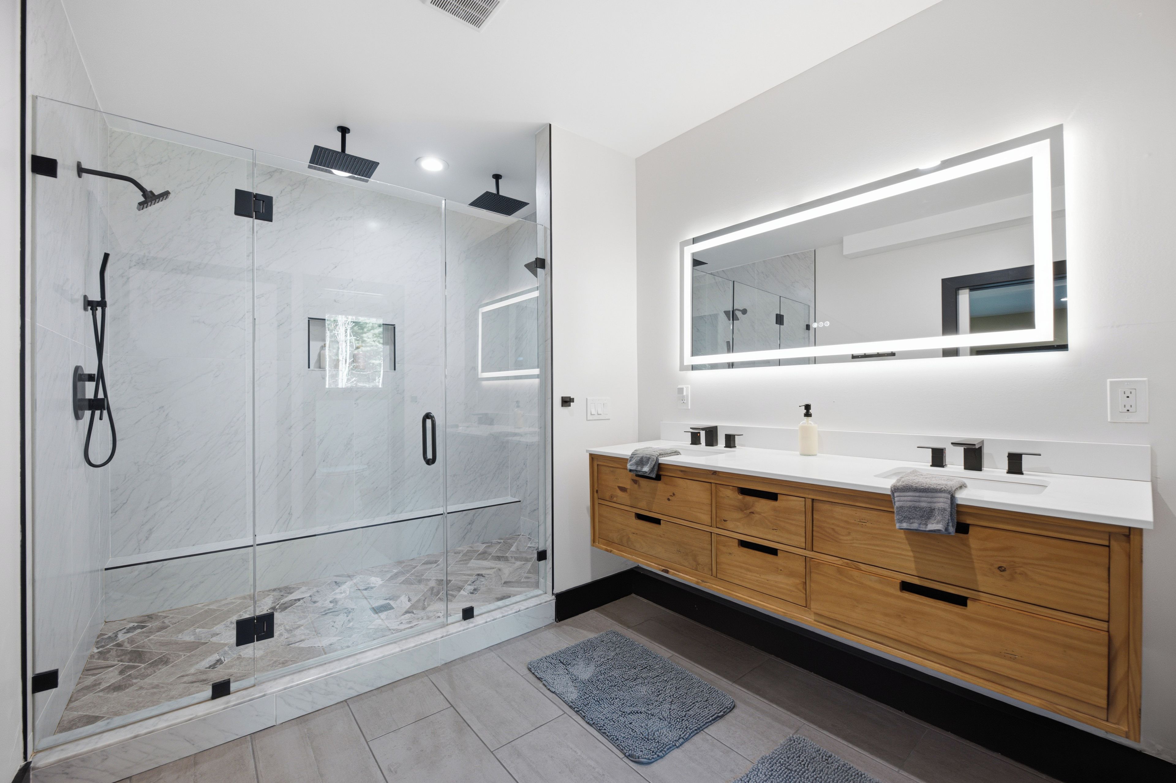Une salle de bain moderne avec une douche à parois de verre, un grand miroir et des meubles en bois.