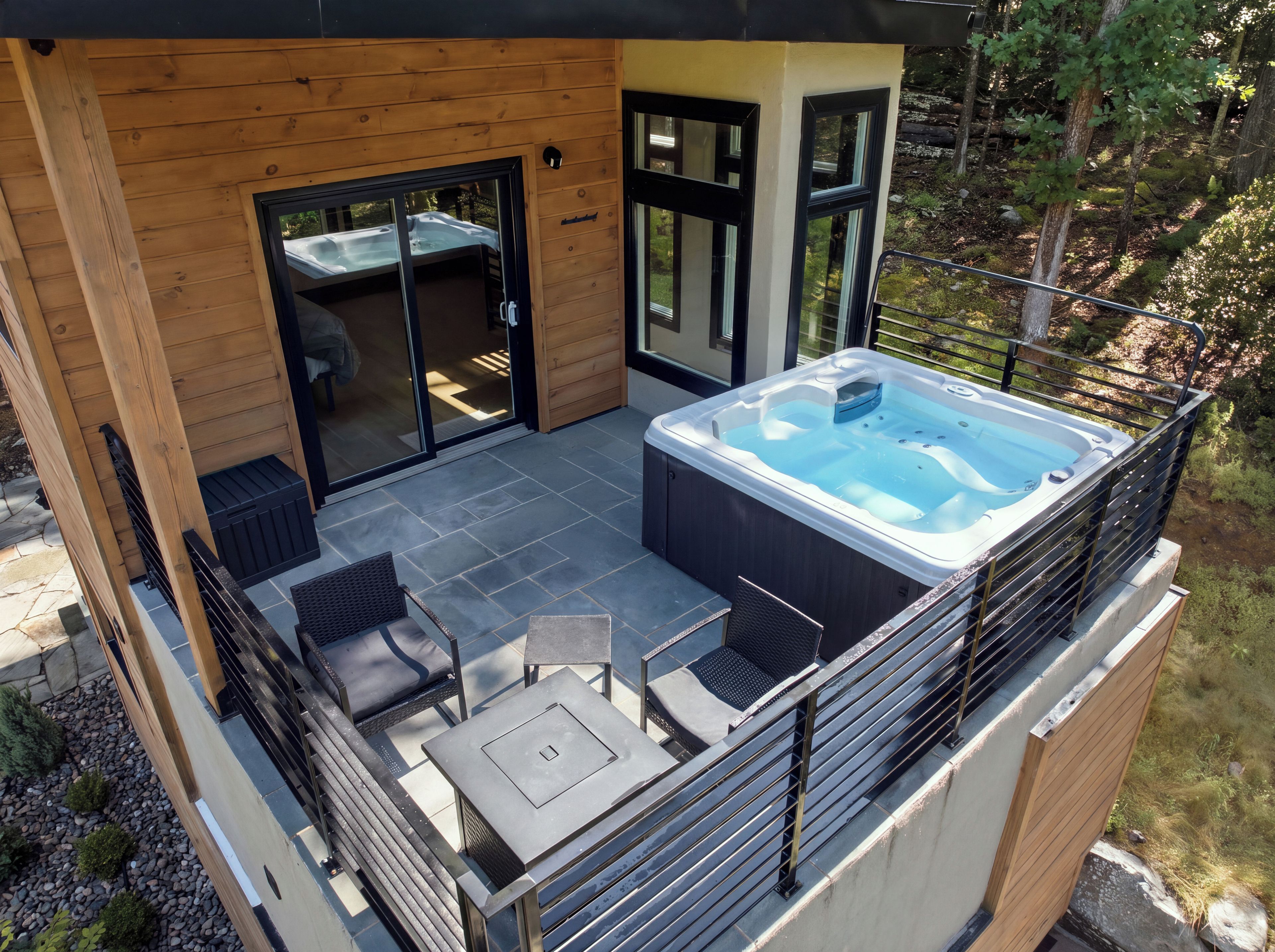 A hot tub on a deck with a wooden exterior and glass doors leading to an interior space.
