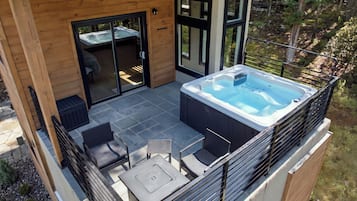 Una vasca idromassaggio su un patio con rivestimento in legno e porte vetrate che danno su un ambiente interno.
