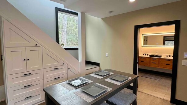 A dining area with a dark wooden table and chairs, a staircase, and a kitchen visible through an open doorway. - Secluded modern cabin with hot tub (Eldred)