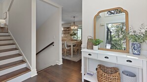 A staircase leading to a dining area with a chandelier, a large mirror, and wicker baskets on a console table.