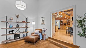 Un salon moderne avec un fauteuil en cuir, des étagères en bois et un escalier menant à un espace cuisine.