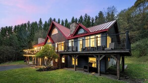 Une maison en bois à plusieurs étages, dotée d’un balcon et entourée d’une forêt.