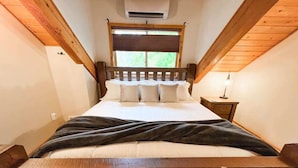 Une chambre à coucher avec un lit en bois, une fenêtre avec des stores, une table de chevet et un appareil de climatisation.