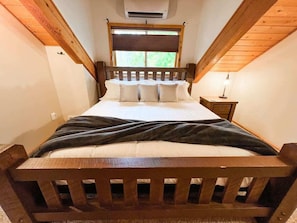Makuuhuoneessa on puinen sängynrunko, ikkunassa sälekaihtimet, yöpöytä ja ilmastointilaite.