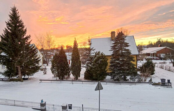 A snow-covered landscape with a large building featuring a distinctive roof, surrounded by trees and a clear sky.