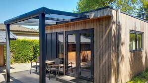A modern wooden structure with a glass door and a covered patio area with chairs. - Nice home in Heinkenszand with WiFi (Heinkenszand)