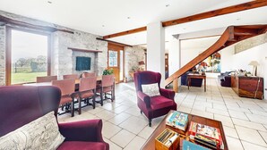 Un salón amplio con una pared de piedra, una escalera de madera y un comedor con mesa y sillas.