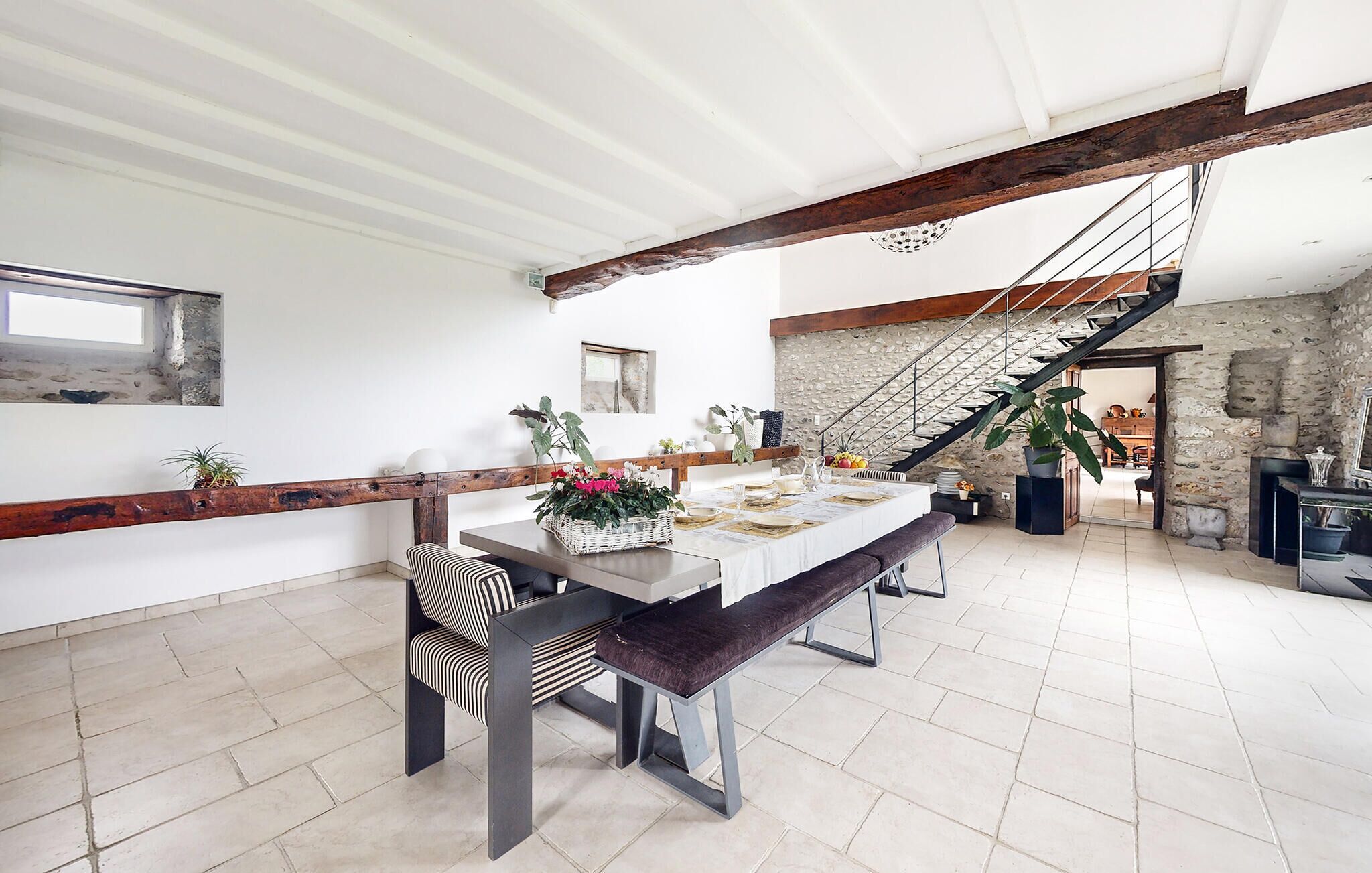 A spacious dining area with a long table set for four, a bench, and a staircase leading to an upper level.