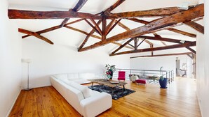 Un loft amplio con vigas de madera a la vista, un sofá blanco, una mesa de comedor y una escalera que conduce a un nivel superior.