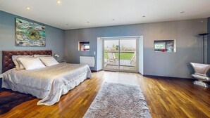 Un dormitorio espacioso con una cama grande, vistas a una terraza exterior por una puerta corrediza de vidrio y una obra de arte moderna en la pared.