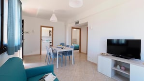 A modern living room with a sofa, dining table, chairs, a TV, and a kitchen in the background. - 2 bedroom lovely home in Marina di Modica (Marina di Modica)