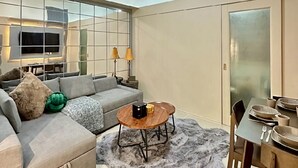 Una sala de estar moderna con un sofá gris, una mesa de centro redonda y un comedor con una mesa dispuesta para dos.