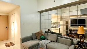 Una sala de estar moderna con un sofá gris, dos mesas de madera, un tapete y un ventanal con vistas a una cocina y comedor.