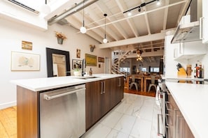 Uma cozinha moderna com ilha central, eletrodomésticos de aço inoxidável e uma escada que leva a um andar superior.