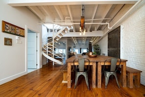 Uma sala de jantar espaçosa com mesa de madeira e cadeiras de metal, uma escada em espiral e uma parede de tijolos brancos.
