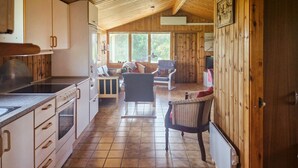 A kitchen with wooden cabinets, a stove, and a dining area with a table and chairs. - Three bedroom nice home in Løkken (Løkken)