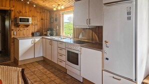 A compact kitchen with wooden walls, a microwave, a stove, a sink, and a refrigerator. - Three bedroom nice home in Løkken (Løkken)