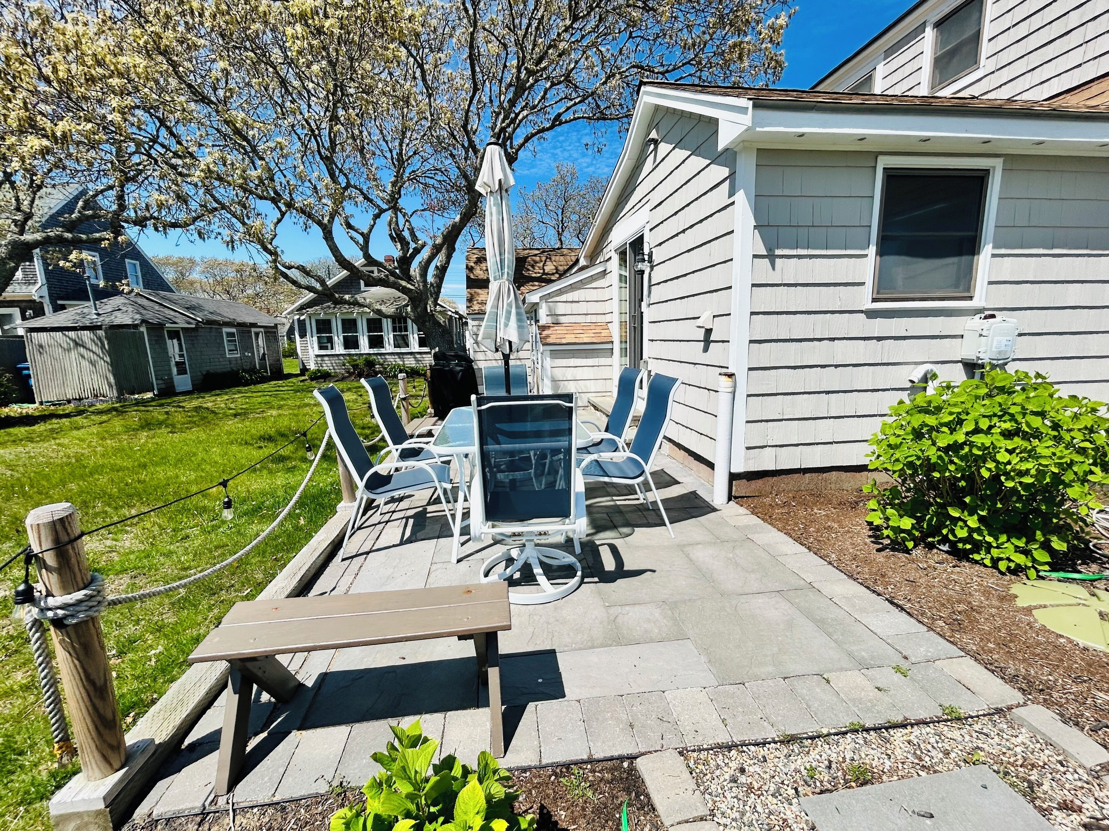 A patio with a table and chairs, a wooden bench, and a garden area with a hedge.