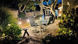 Un espace extérieur aménagé en terrasse, avec une table et des chaises, entouré de plantes et d’arbres.