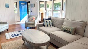 Un salon avec un canapé beige, une table basse ronde, une porte bleue et une fenêtre donnant sur un beau paysage.