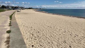 Une vaste plage de sable, avec une promenade en béton et une vue dégagée sur l’océan.