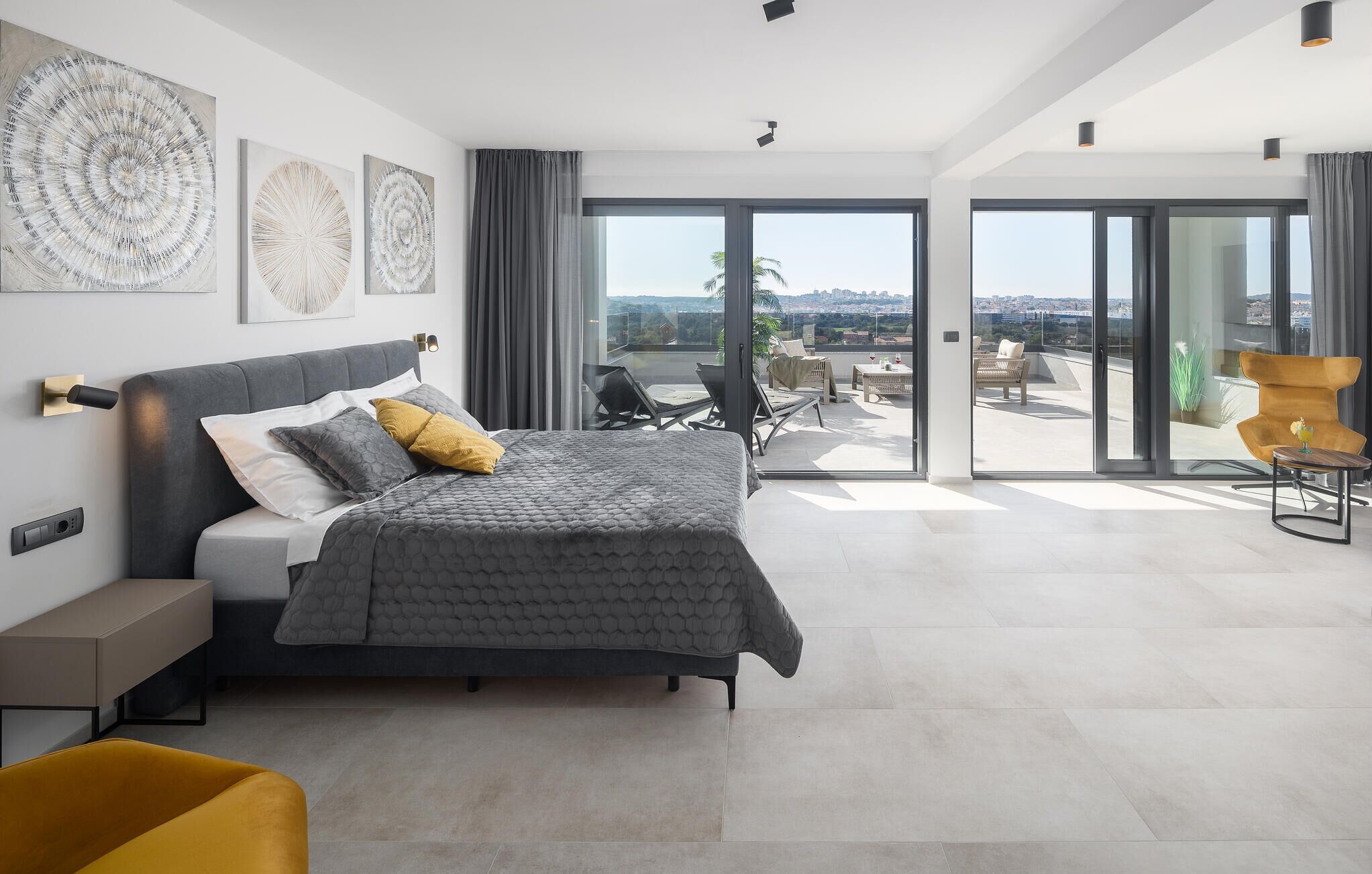 A modern bedroom with a large bed, a sofa, and a balcony with a view.