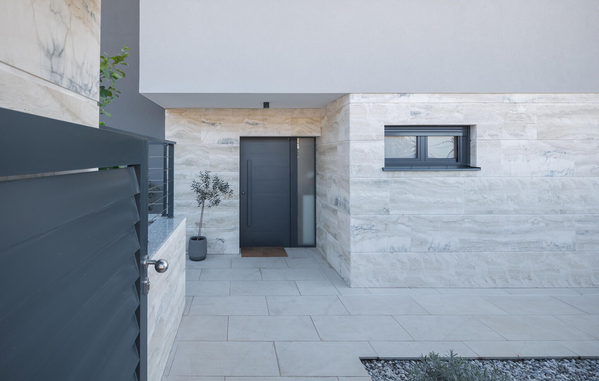 Un bâtiment moderne avec une porte d’entrée sombre, une petite fenêtre et un pot de fleurs.