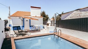 A swimming pool with a tiled deck, a barbecue area, and a small patio with chairs and a table.