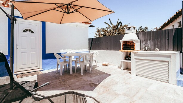 A patio with a table and chairs, a barbecue grill, and a large umbrella.