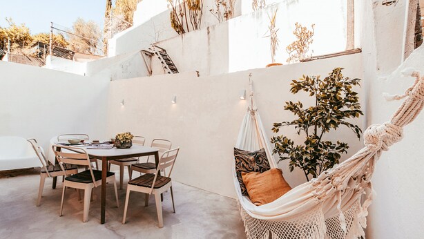 Un patio con una mesa redonda y sillas, una hamaca y una planta en maceta.