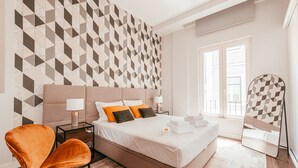 A modern hotel room with a geometric patterned wall, a large bed with white linens, a brown armchair, and a bedside table with lamps. - Elegant & Sophisticated by GT House (Lisbon)