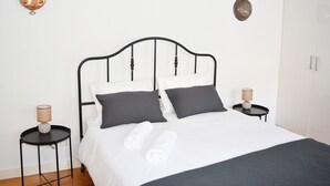 A neatly made bed with white and dark gray linens, two bedside tables with lamps, and a white wardrobe in a minimalist room. - Kalathos House 4 Apartment by GT House (Lisbon)