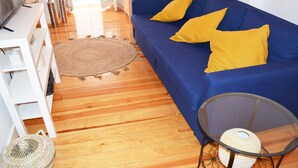 A living room with a blue sofa, yellow cushions, a round woven rug, a glass coffee table, and a white TV stand. - Kalathos House 4 Apartment by GT House (Lisbon)