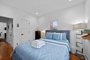 Un dormitorio moderno con una cama, una lámpara de noche, un ventanal con persianas y una puerta.