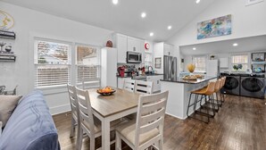 A modern kitchen with white cabinets, a dining area with a wooden table and chairs, and a laundry area with a washing machine and dryer.