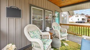 A covered porch with wicker chairs, a small table, and a hanging sign.