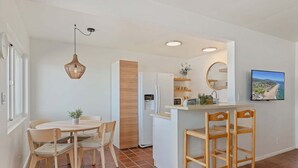 A compact kitchen with a dining area, a refrigerator, a sink, and a television mounted on the wall.