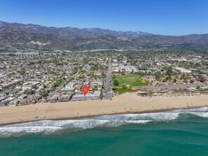 Vista aérea de una ciudad costera con playa, zonas residenciales y montañas al fondo.