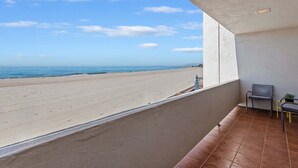 A balcony with a view of a beach, a chair, and a small table.