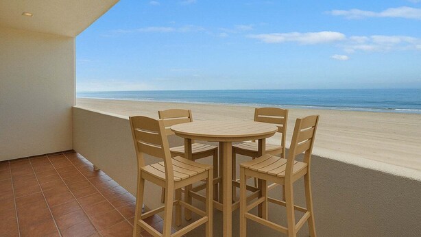 A balcony with a table and chairs, overlooking a beach.