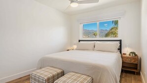 A bedroom with a bed, two bedside tables, a nightstand, a ceiling fan, and a window with a view of mountains.