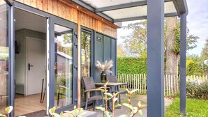 Una casa moderna con puerta de entrada de vidrio, fachada de madera y un pequeño patio con mobiliario exterior.