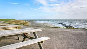 Una mesa de picnic en un sendero pavimentado junto al mar, con costa rocosa y olas.