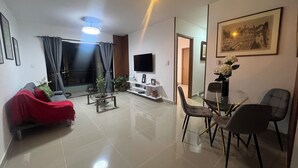 Ein modernes Wohnzimmer mit einem roten Sofa, einem Glastisch, einem Fernseher und einem Essbereich mit Stühlen.