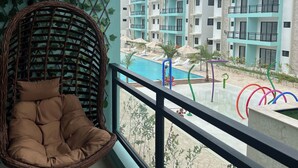 Ein Balkon mit Korbstuhl, Blick auf einen Swimmingpool und ein Gebäude mit mehreren Balkonen.