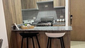 Eine moderne Küche mit Holzschränken, einem Gasherd, zwei Barhocker und einer Arbeitsplatte mit Küchenutensilien.